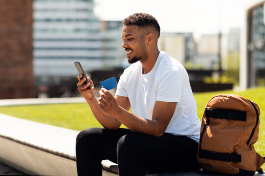 Technology, online payment and people concept. Excited black man with smartphone and credit card ordering goods outdoors
