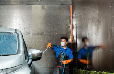 Worker with gloves spraying soap foam and washing a vehicle in professional car wash station.