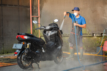Worker using a hose for detailed cleaning. Spraying and washing a motorbike in professional car...