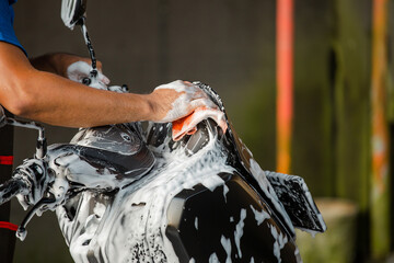 Worker washing a motorbike with foam soap in car wash station.