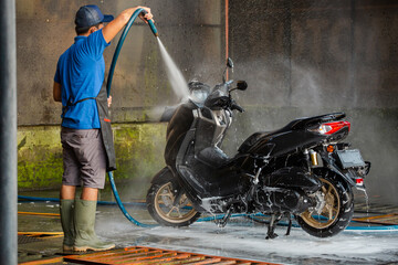 Worker using a hose for detailed cleaning. Spraying and washing a motorbike in professional car wash station. - 510429096