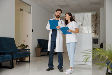 Doctor and nurse colleagues discussing patient diagnosis stand in clinic hall