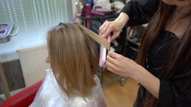 A hairdresser curls woman's hair with the hair straightener. Hair curling.