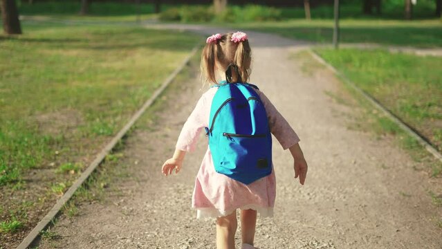 back to school. a little girl with a backpack runs through the green park to school along the path. education kid dream concept. a small child with sun a backpack back view runs the park to school