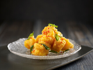 Crispy-fried Crystal Prawns with Salted Egg Yolk served in a dish isolated on cutting board side view on dark background