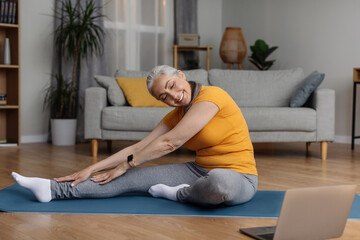 Athletic senior woman stretching her leg on yoga mat, workig out at home, keeping flexible, leading healthy lifestyle