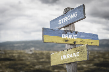strong brave ukraine text quote on wooden signpost outdoors in nature. War in ukraine concept.