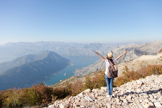 Traveler with backpack on mountain top. Happy woman with raised arms in autumn landscape. Tourist enjoying travel, freedom, vacation. Concept of wanderlust, adventure. Rear view