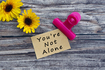 You are not alone text on torn paper with paper clip holder on wooden surface.