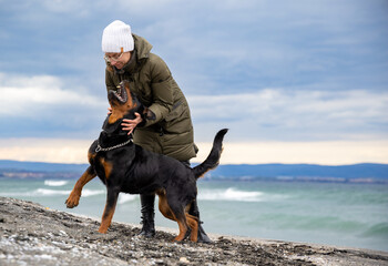Woman fooling around with rottweiler dog in cold weather on the beach
