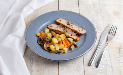 Sliced roasted pork meat in plate with vegetables on wooden table with rosemary and peppers.