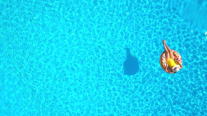 Aerial view of a woman in yellow swimsuit lying on a donut in the pool