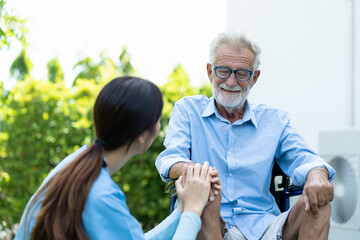 Caring Asian nurse taking care of old man in wheelchair at the park. Friendly female doctor caring elderly man in wheelchair. Happy woman with her caregiver at nursing home garden.
