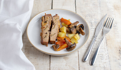 Sliced roasted pork meat in plate with vegetables on wooden table with rosemary and peppers.
