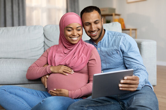 Beautiful Happy Black Pregnant Muslim Family Relaxing With Digital Tablet At Home