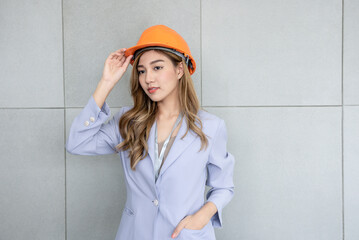 Portrait images of an Asian business woman, attractive and young, wearing and holding worker helmet, with wall background, to business and engineer concept.
