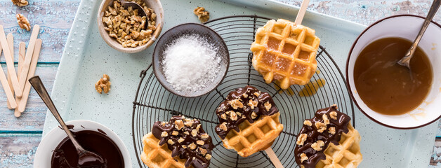 Narrow view of decorated waffle pops with various toppings all around.