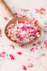 See salt wih with dried flower petals in wooden scoop on pink marble table