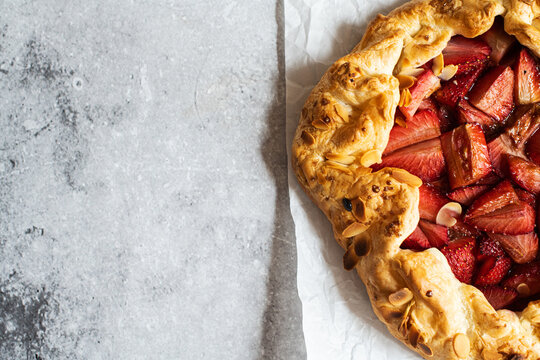 Strawberry summer galette with puf pastry and almond flakes on gray background. Copy space.