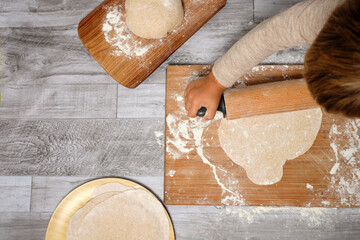 Top view of boy kneading pizza with wooden rolling pin surrounded by flour. copy space