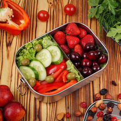 Metal snack box with olives, cucumbers, lettuce, sweet peppers and fruits on a wooden background