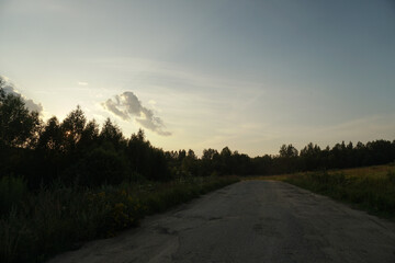 Rural road through the field. Beautiful nature landscape, blue sky at dusk.