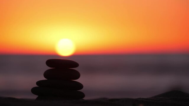 Stack of pebble stones, sandy ocean beach, sunset sky. Rock balancing in sun light, sea water waves. Stones staking in pyramid pile. Zen meditation and harmony in balance. Calm tranquil atmosphere.
