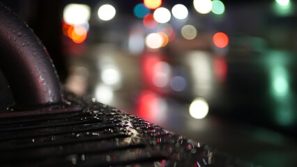 Car traffic lights bokeh, reflection on bus stop bench in rainy weather. Water rain drops on wet metal, city street in Clifornia, USA. Rainfall at night. Defocused abstract Seamless looped cinemagraph - obrazy, fototapety, plakaty