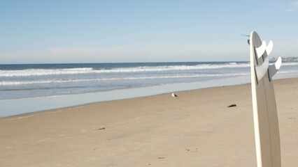 Surfboard for surfing standing on beach sand, California coast, USA. Ocean wave and white surf...