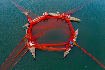 Local fishermen are fishing in river with huge net. Aerial View taken with drone. - obrazy, fototapety, plakaty