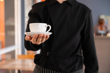 Professional barista hand holding white cup of coffee. .