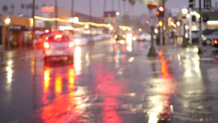 Fototapeta na wymiar Cars lights reflection on road in rainy weather. Rain drops on wet asphalt of city street in USA, water raindrops falling on sidewalk. Palm trees and rainfall, twilight dusk. Ocean Beach, California.