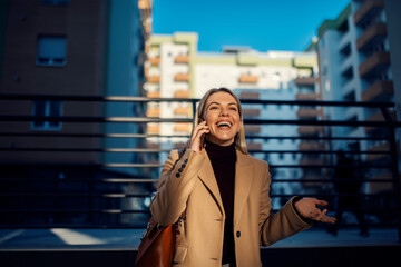 A happy woman speaking on the phone on city street.