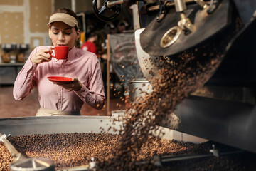 A coffee factory supervisor drinking fresh coffee next to a roasting machine.