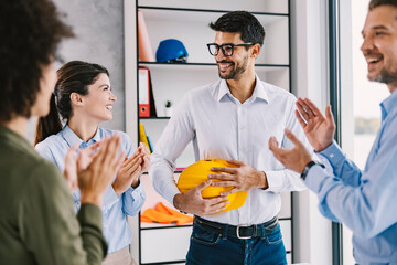 A successful architect in the office smiling at the colleagues who are applauding for achievement.