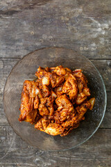 Pieces of chicken in sauce fried in a glass plate on a dark wooden table.
