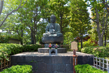 Buddha statue in the green park, surrounded by trees. Buddha wrote in Chinese. Flowers in front of the Buddha statue.