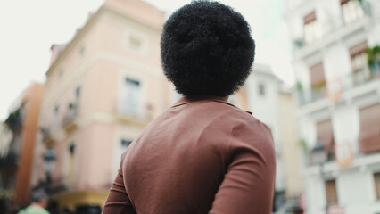 Back view of dark haired African woman standing on a street. Att