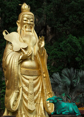 Gold colour of Daode Tianzun statue at the temple, beside the rainforest/mountain.