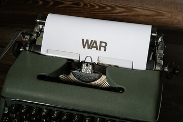 War is written in large letters on a white piece of paper on an old army green typewriter.