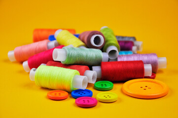 Set of buttons and Spools with multicolored threads on a yellow background. Blurring background.