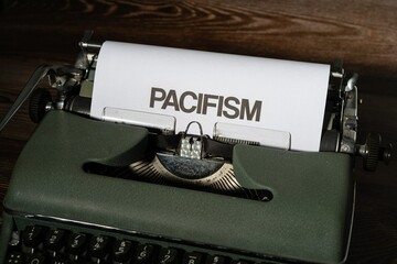 Pacifism is written in large letters on a white piece of paper on an old army green typewriter.