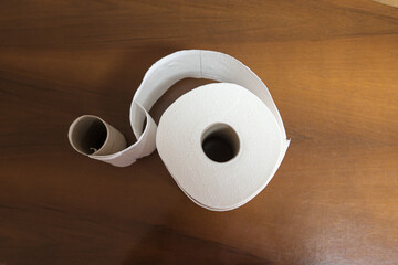 top view of an empty toilet paper roll intertwined with a new toilet paper roll on a dark wooden base