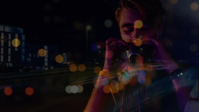 Animation of blurred night road traffic over caucasian man playing harmonica on concert