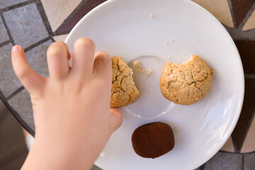 The view from above on the hand of the child taking homemade cookies from a white plate.
