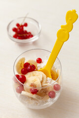 Cottage cheese with banana slices and red currant berries in a glass cup. Delicious and healthy breakfast, located in a glass cup on a light background