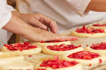 Obraz na płótnie Canvas Baker makes filled pies from yeast dough, filling pies with strawberries. Work in bakery. Selective focus.