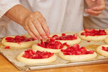 Baker makes filled pies from yeast dough, filling pies with strawberries. Work in bakery. Selective focus.