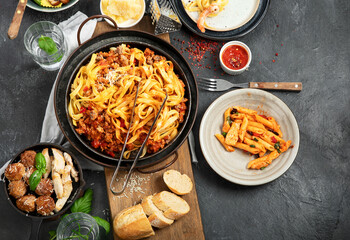Assortment of Italian pasta with traditional sauces for dinner on dark background. Homemade food concept