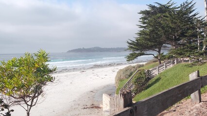 Ocean sandy beach, Carmel, Monterey nature, California coast USA. Big foamy sea water waves crashing on shore. Vacations waterfront beachfront resort. Sunny weather, wooden stairs, steps or stairway.
